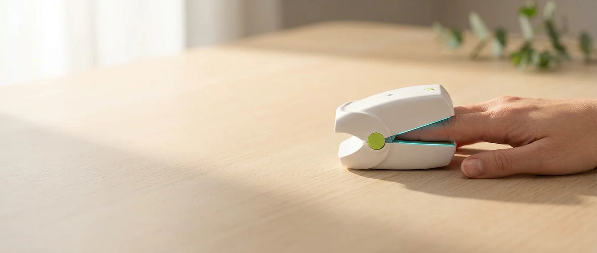 A hand resting on a table, the device clipped to one fingertip